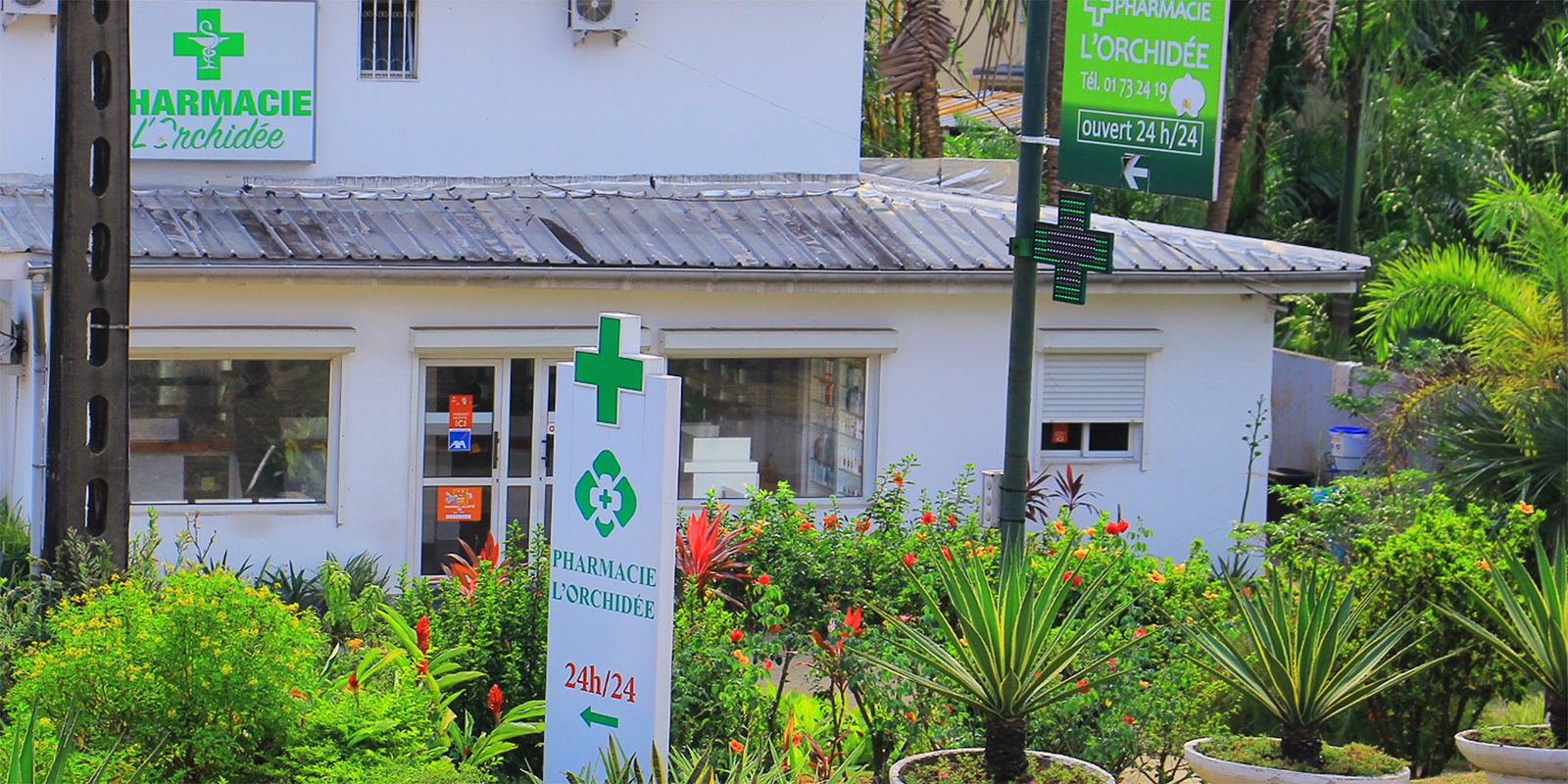 Façade de la Pharmacie L'Orchidée, son jardin et l'enseigne à croix verte
